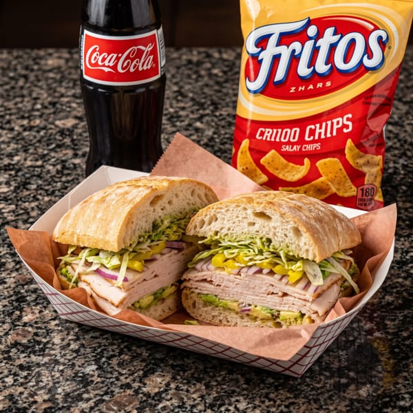 A turkey sandwich with avocado, lettuce, onions, and peppers, with a Coca-Cola and Fritos chips.